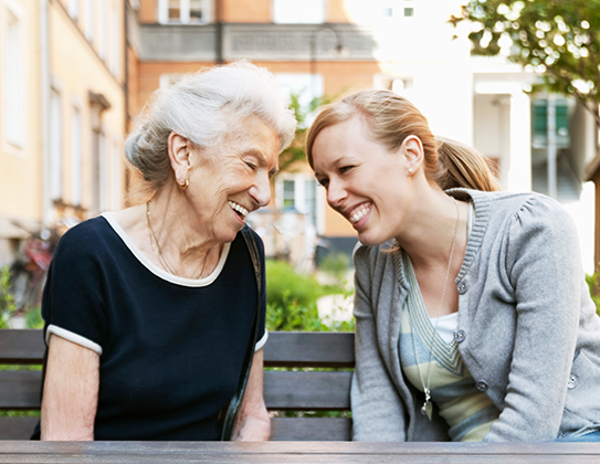 A woman laughing on a park bench with an elderly woman