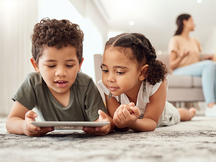 Two young siblings lying on the floor watching a tablet.